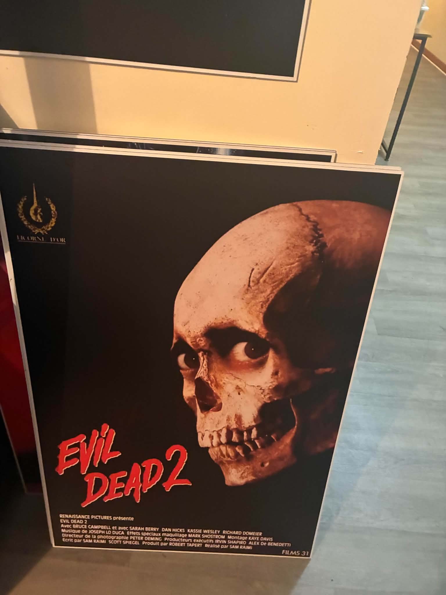 Photo of the Evil Dead 2 poster print dominated by a giant cracked skull with glowing red eyes above the title